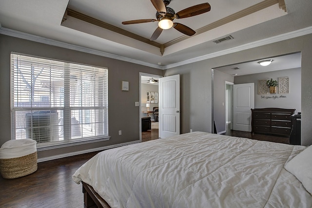 bedroom with wood finished floors, visible vents, baseboards, ornamental molding, and a raised ceiling