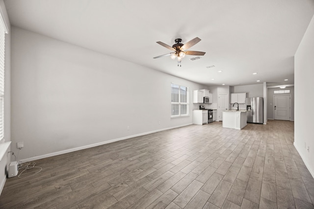 unfurnished living room featuring baseboards, visible vents, ceiling fan, wood finished floors, and a sink