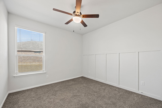 spare room featuring a wainscoted wall, dark carpet, a decorative wall, and ceiling fan