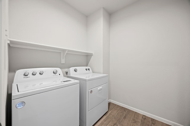 clothes washing area with laundry area, baseboards, washing machine and clothes dryer, and wood finished floors