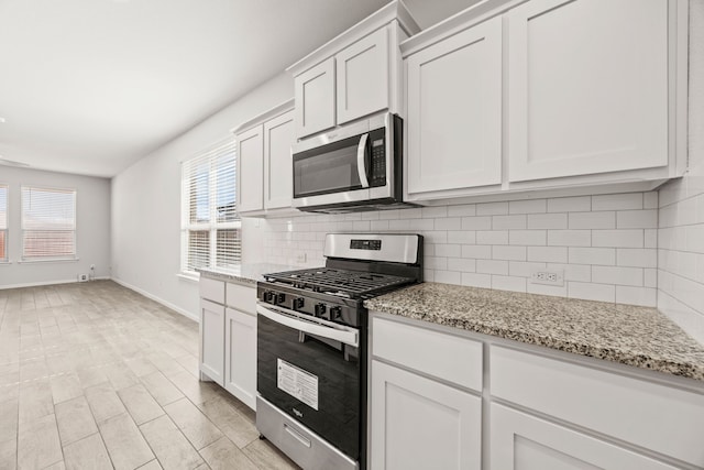 kitchen with appliances with stainless steel finishes, white cabinetry, backsplash, and light stone counters