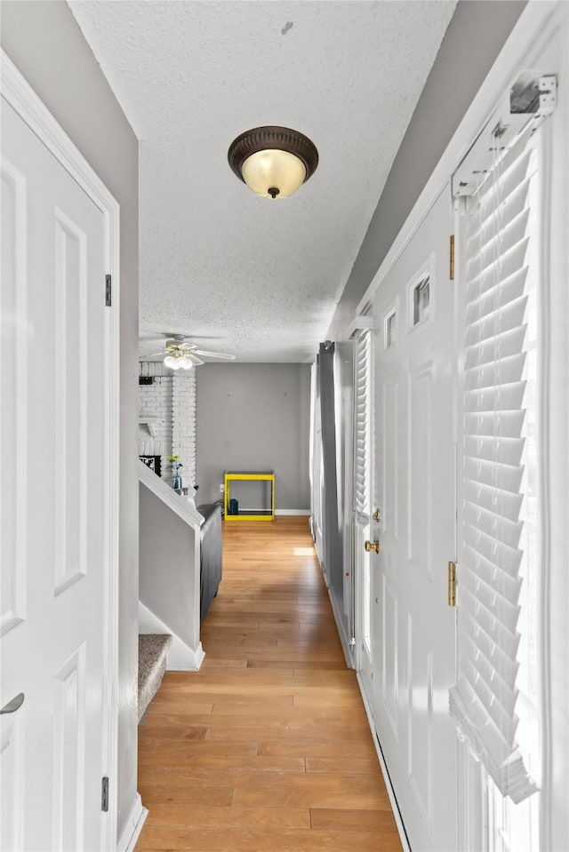 hall with baseboards, a textured ceiling, light wood finished floors, and stairs