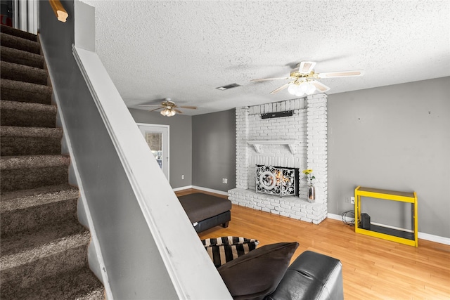 stairs with ceiling fan, a fireplace, wood finished floors, and visible vents