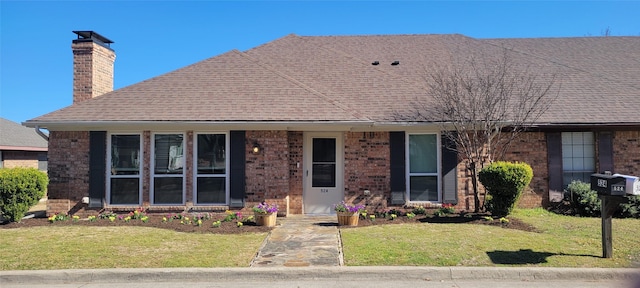 view of front facade featuring brick siding, a shingled roof, a chimney, and a front yard