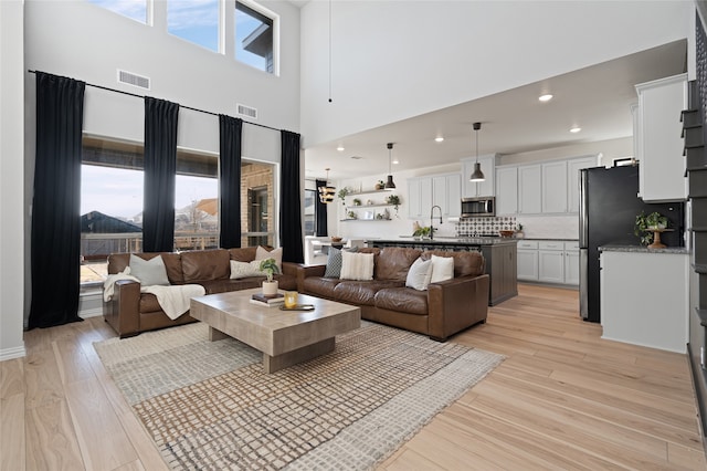 living room featuring recessed lighting, visible vents, a high ceiling, and light wood finished floors