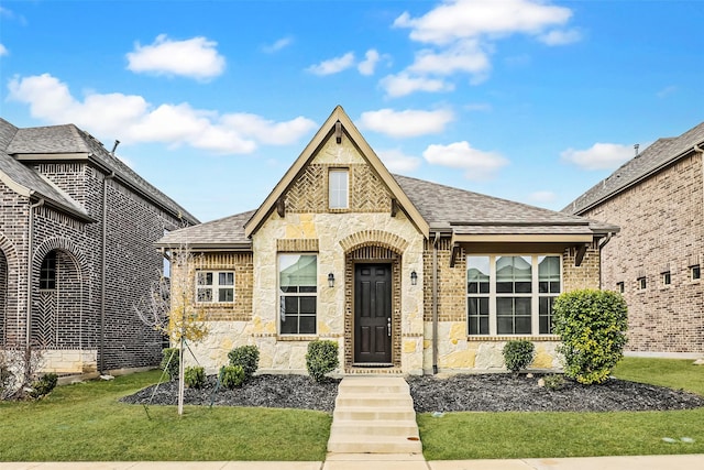 view of front facade with a shingled roof, stone siding, and a front lawn