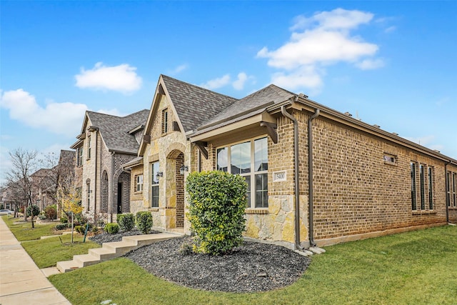 view of side of home with stone siding, brick siding, a lawn, and roof with shingles