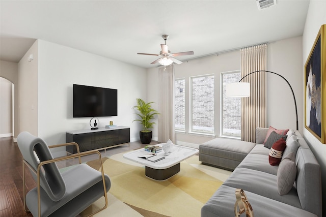 living area with arched walkways, wood finished floors, visible vents, baseboards, and a ceiling fan