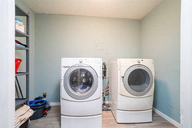 clothes washing area featuring light wood-style floors, laundry area, washer and clothes dryer, and a textured ceiling