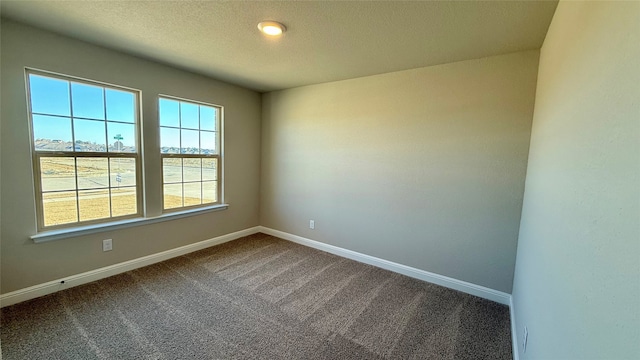 empty room featuring dark colored carpet, a textured ceiling, and baseboards