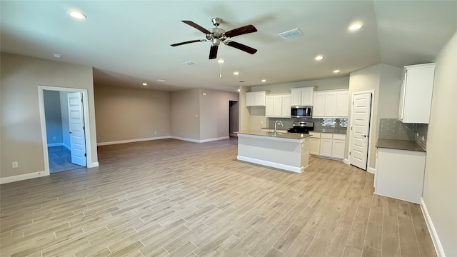 kitchen with tasteful backsplash, appliances with stainless steel finishes, light wood-style floors, open floor plan, and white cabinetry