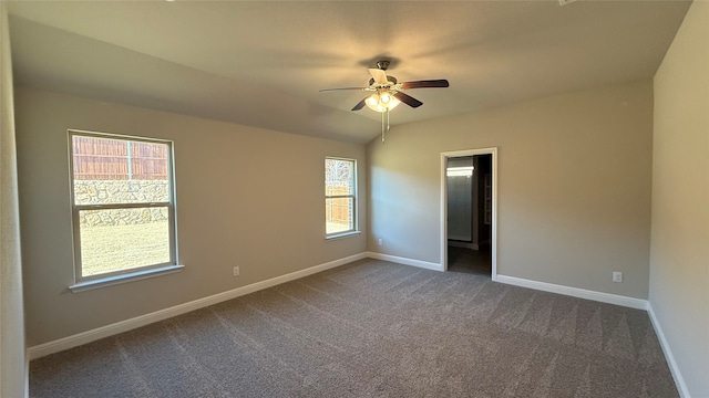 unfurnished room with a healthy amount of sunlight, dark carpet, and baseboards