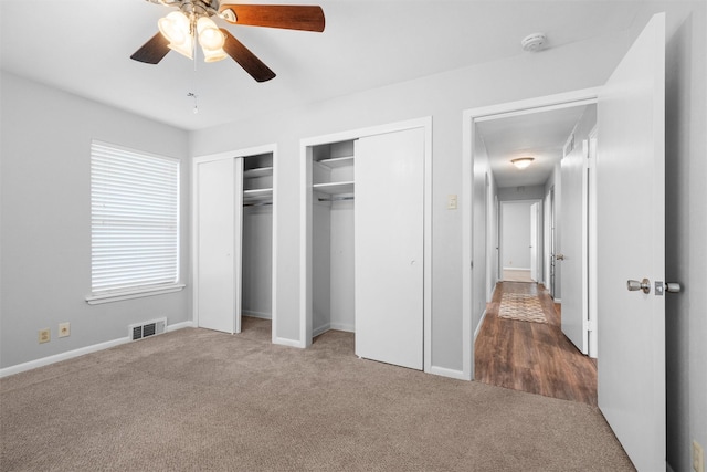 unfurnished bedroom featuring baseboards, visible vents, a ceiling fan, carpet floors, and two closets