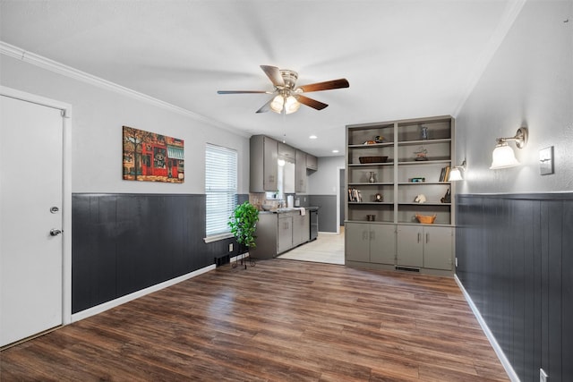 interior space featuring a wainscoted wall, ceiling fan, ornamental molding, and wood finished floors