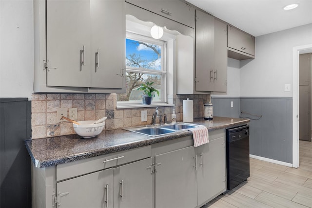 kitchen with black dishwasher, dark countertops, a wainscoted wall, gray cabinetry, and a sink