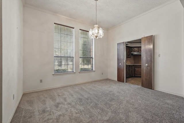 spare room featuring a textured ceiling, ornamental molding, carpet flooring, and an inviting chandelier