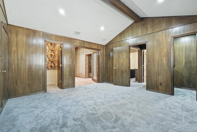 unfurnished bedroom with lofted ceiling with beams, carpet floors, wood walls, and visible vents