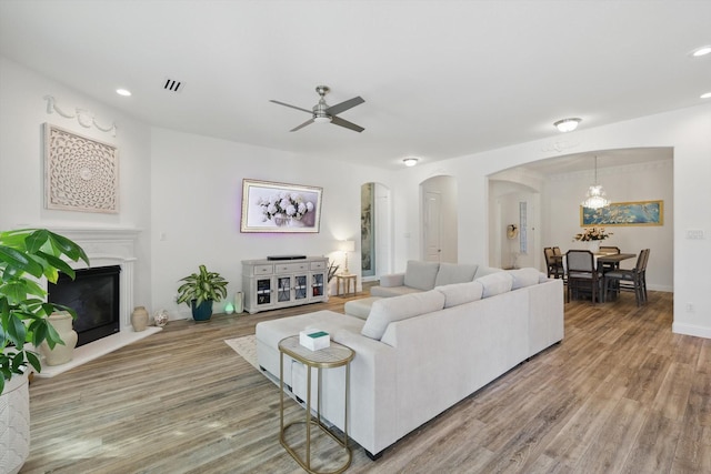 living room featuring arched walkways, wood finished floors, a glass covered fireplace, and visible vents