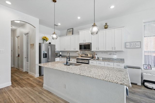 kitchen featuring arched walkways, white cabinets, appliances with stainless steel finishes, light wood-type flooring, and a sink