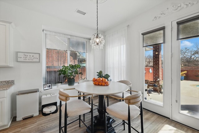 dining room featuring light wood finished floors, plenty of natural light, visible vents, and a notable chandelier