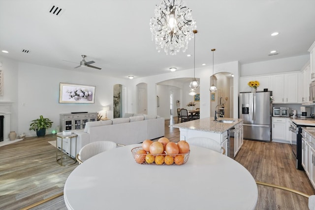 dining space featuring arched walkways, ceiling fan with notable chandelier, wood finished floors, and recessed lighting