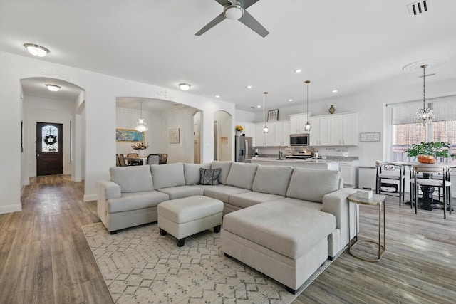 living area with recessed lighting, visible vents, arched walkways, light wood-style flooring, and ceiling fan with notable chandelier