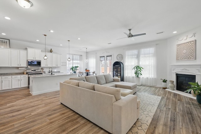 living room with light wood finished floors, recessed lighting, visible vents, and a glass covered fireplace