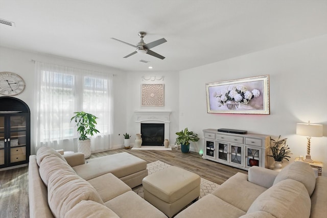 living room featuring ceiling fan, wood finished floors, a glass covered fireplace, and visible vents