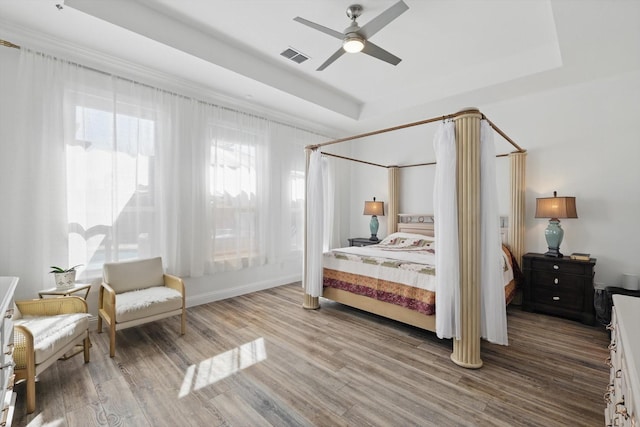 bedroom featuring ceiling fan, a tray ceiling, wood finished floors, and visible vents