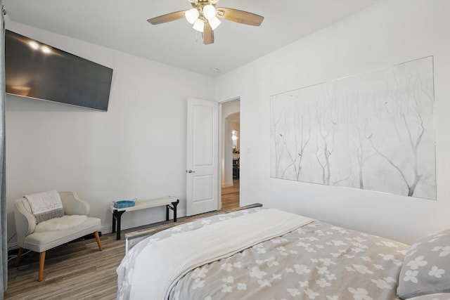 bedroom featuring arched walkways, ceiling fan, and wood finished floors