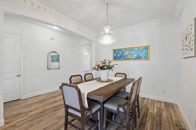 dining area featuring arched walkways, a chandelier, wood finished floors, and baseboards