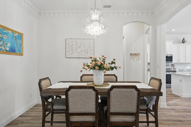 dining space with arched walkways, a notable chandelier, crown molding, light wood-type flooring, and baseboards