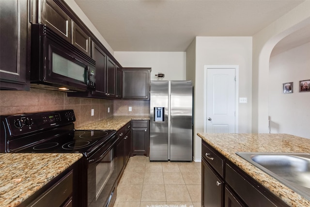 kitchen with arched walkways, light tile patterned floors, tasteful backsplash, a sink, and black appliances