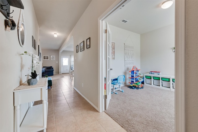 corridor featuring visible vents, light tile patterned flooring, baseboards, and light colored carpet