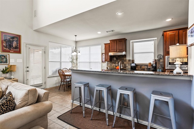 kitchen with light tile patterned floors, visible vents, decorative backsplash, oven, and a kitchen bar