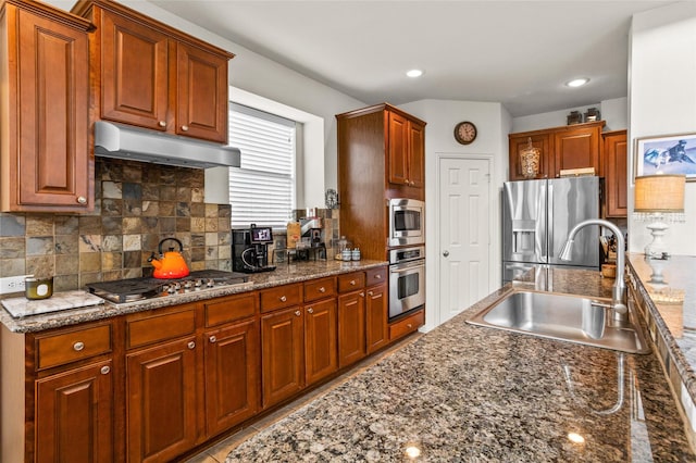 kitchen featuring tasteful backsplash, appliances with stainless steel finishes, a sink, dark stone countertops, and under cabinet range hood