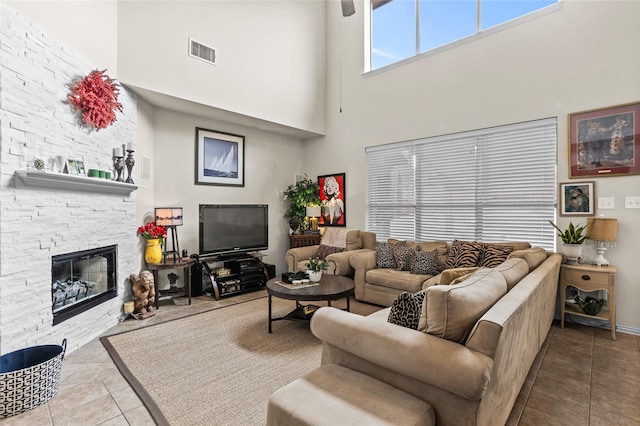 tiled living area with visible vents, a stone fireplace, and a towering ceiling