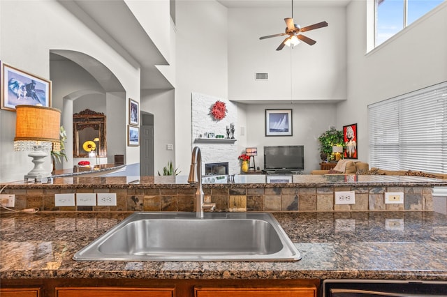 kitchen with visible vents, dark stone counters, open floor plan, a fireplace, and a sink