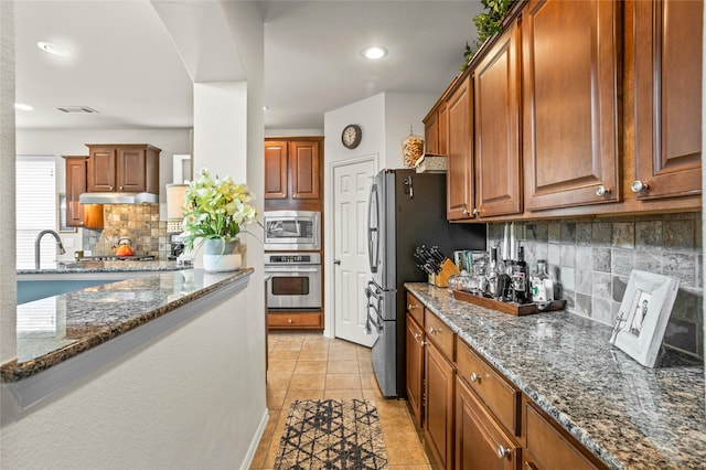 kitchen featuring light tile patterned floors, dark stone counters, stainless steel appliances, and backsplash