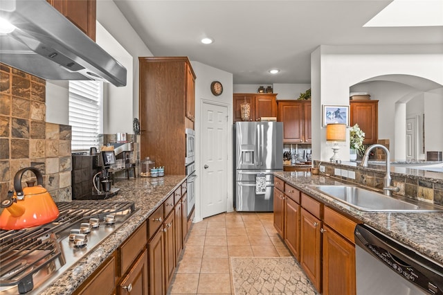 kitchen with under cabinet range hood, a sink, appliances with stainless steel finishes, decorative backsplash, and brown cabinets