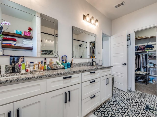 bathroom with double vanity, visible vents, a spacious closet, a stall shower, and a sink