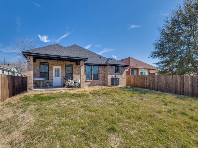 back of property with brick siding, a fenced backyard, central AC unit, and a yard