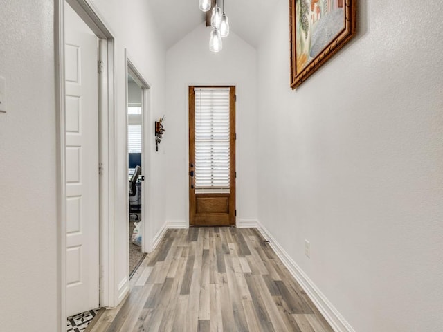 doorway to outside with light wood-type flooring, baseboards, and vaulted ceiling