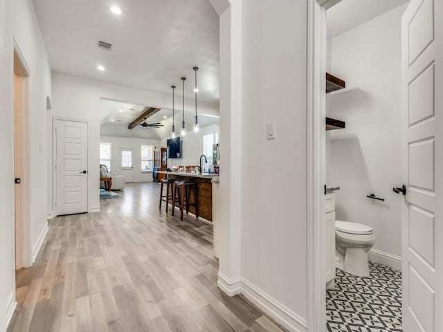 hallway featuring arched walkways, recessed lighting, a sink, baseboards, and light wood-type flooring