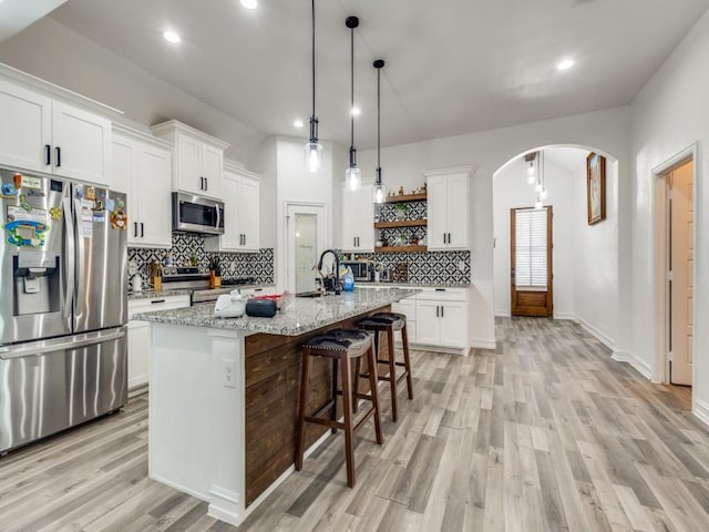 kitchen featuring arched walkways, a breakfast bar, open shelves, stainless steel appliances, and white cabinets