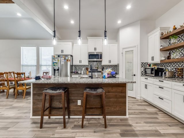 kitchen featuring a center island with sink, white cabinets, appliances with stainless steel finishes, a breakfast bar, and open shelves