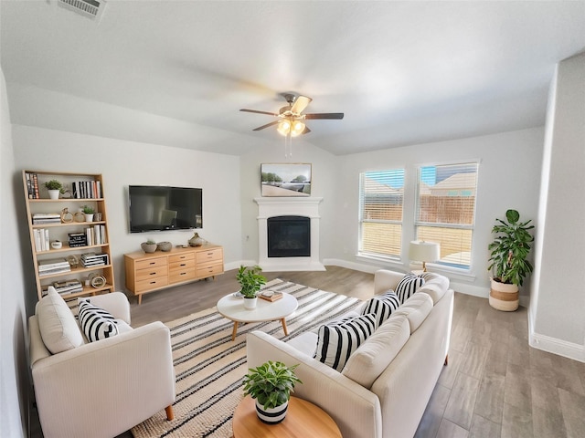 living area with baseboards, visible vents, wood finished floors, vaulted ceiling, and a fireplace