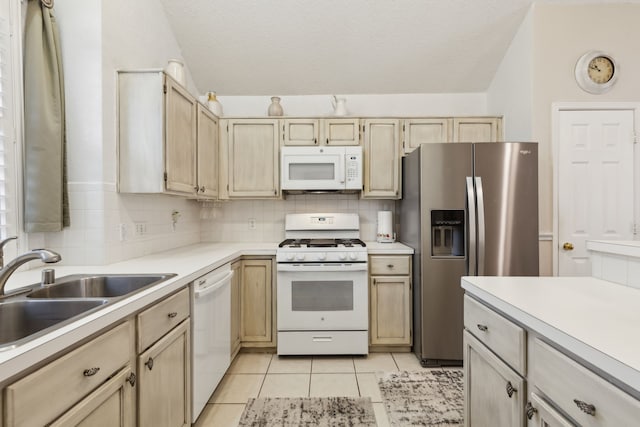 kitchen with a sink, white appliances, light brown cabinets, and backsplash