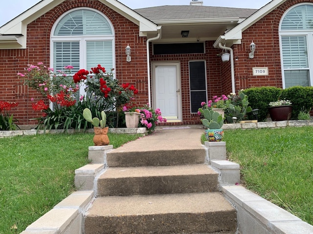 entrance to property with a shingled roof and brick siding