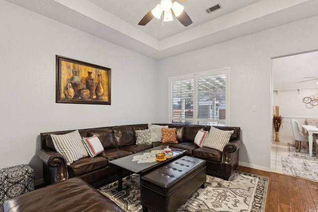 living room featuring ceiling fan, wood finished floors, visible vents, baseboards, and a tray ceiling